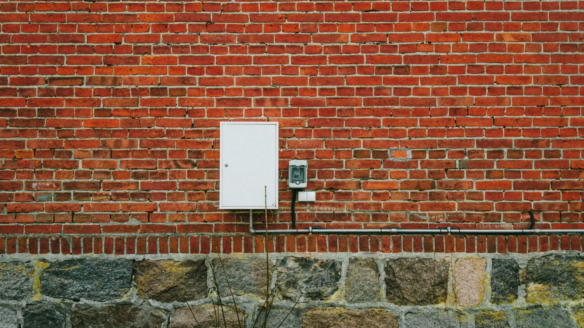 A white meter box fixed to a red brick wall
