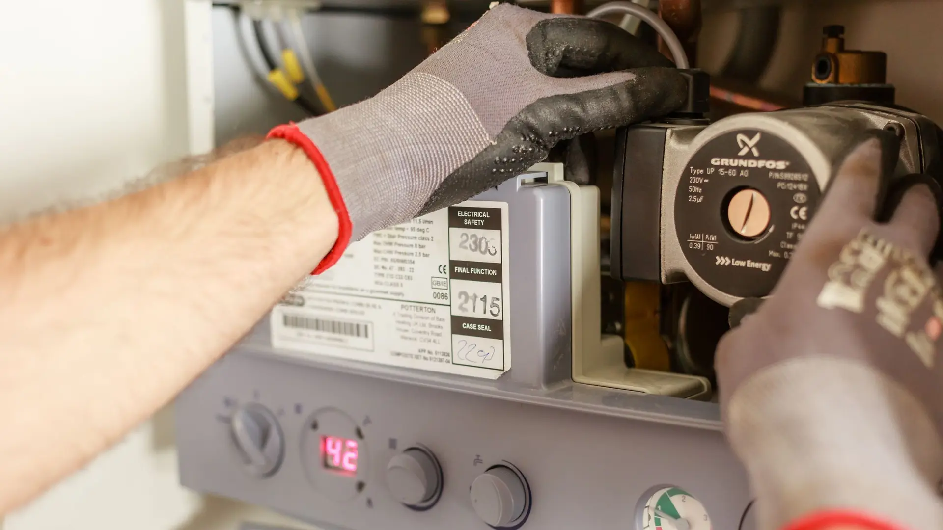 Gloved hands working on a boiler pump and its control panel