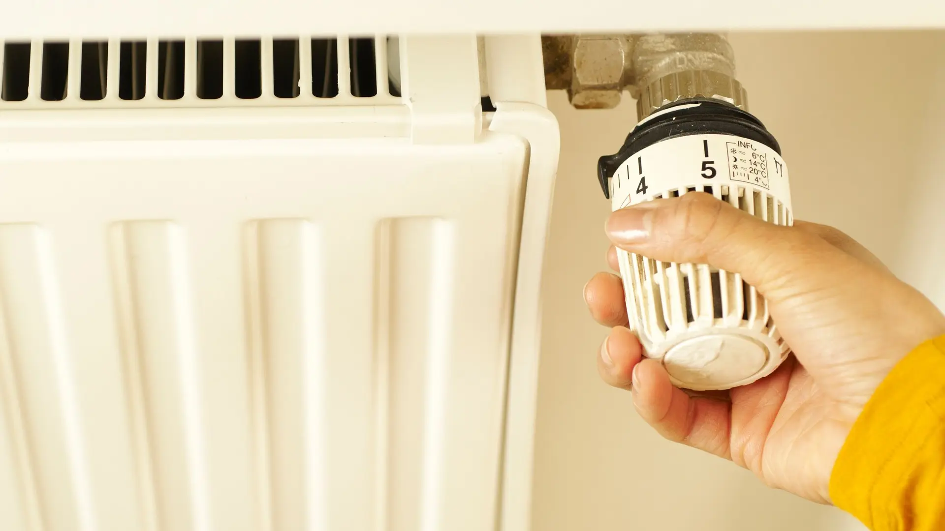 A hand turning the head of a thermostatic radiator valve