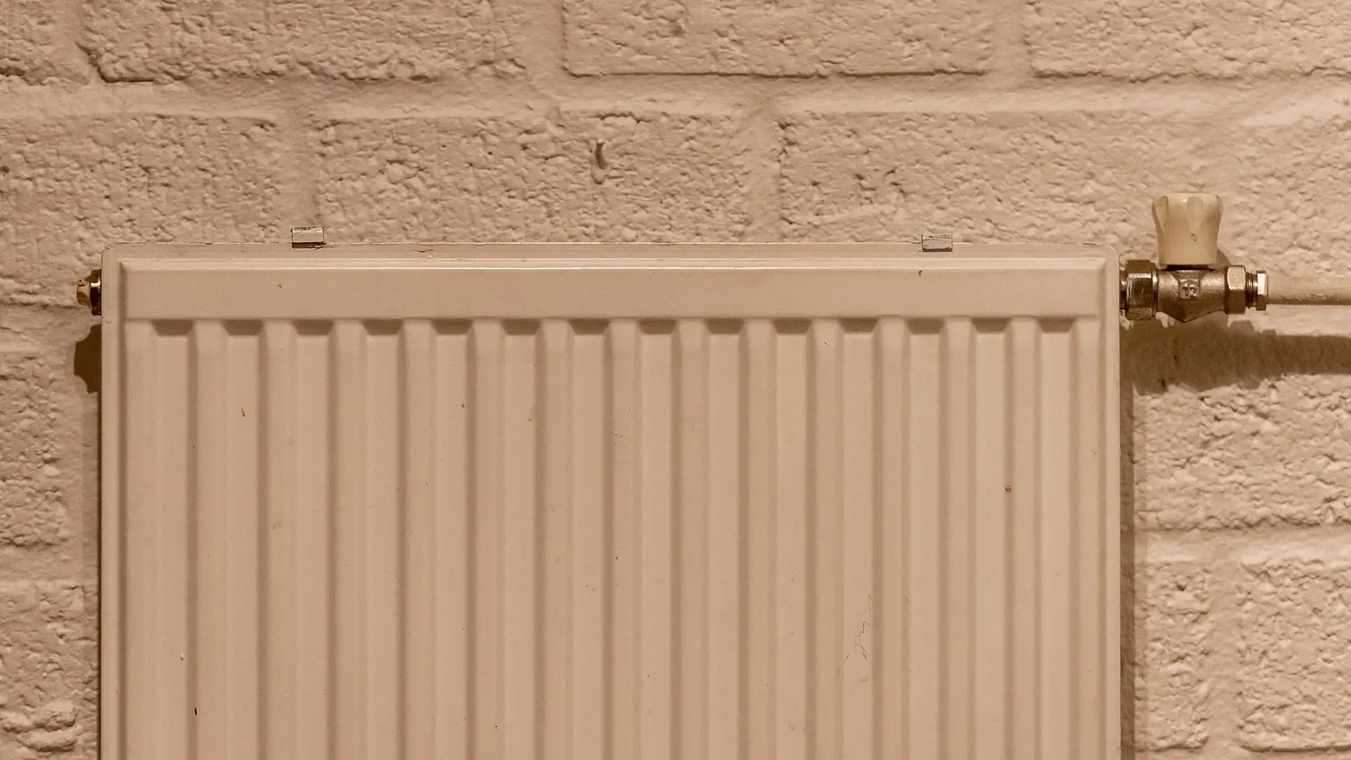 A white panel radiator against a painted brick wall