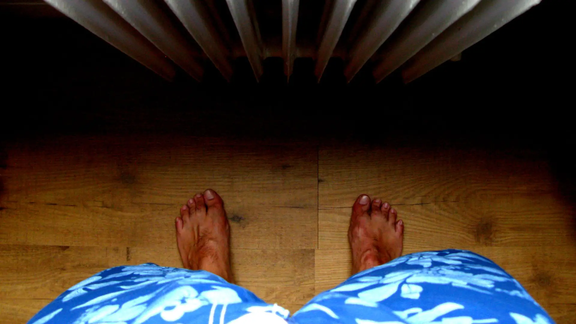 Bare feet on a wooden floor in front of a radiator