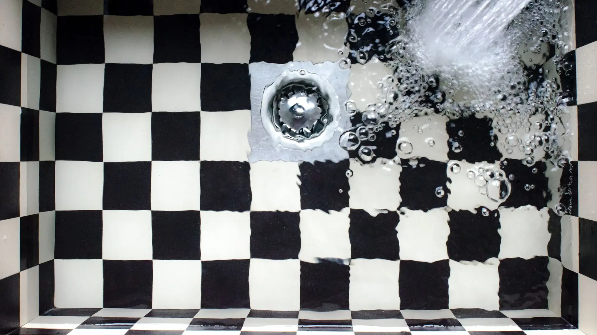 Water swirling into a plughole in a chequered tiled sink