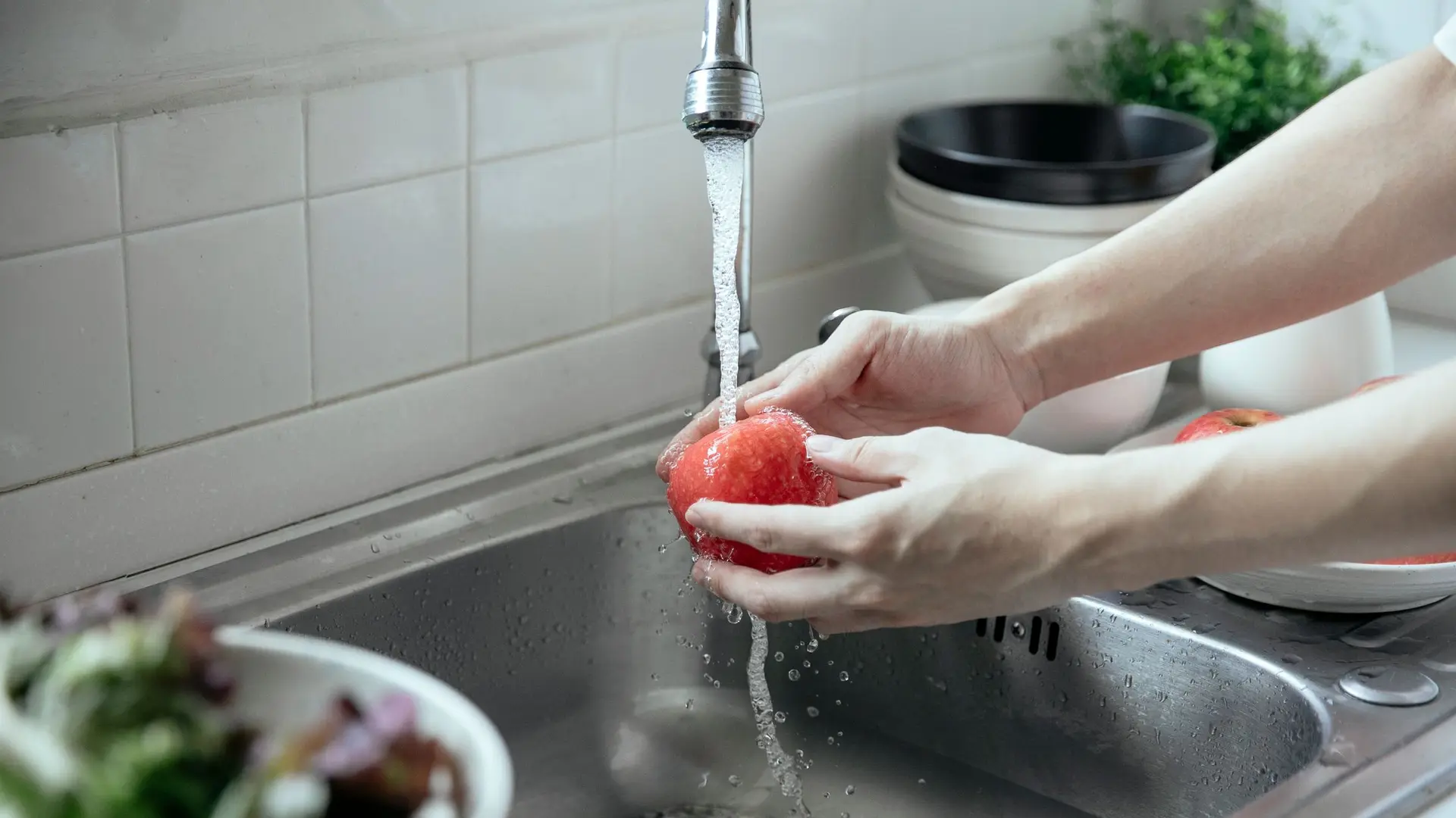Hands washing fruit under a kitchen tap over a sink