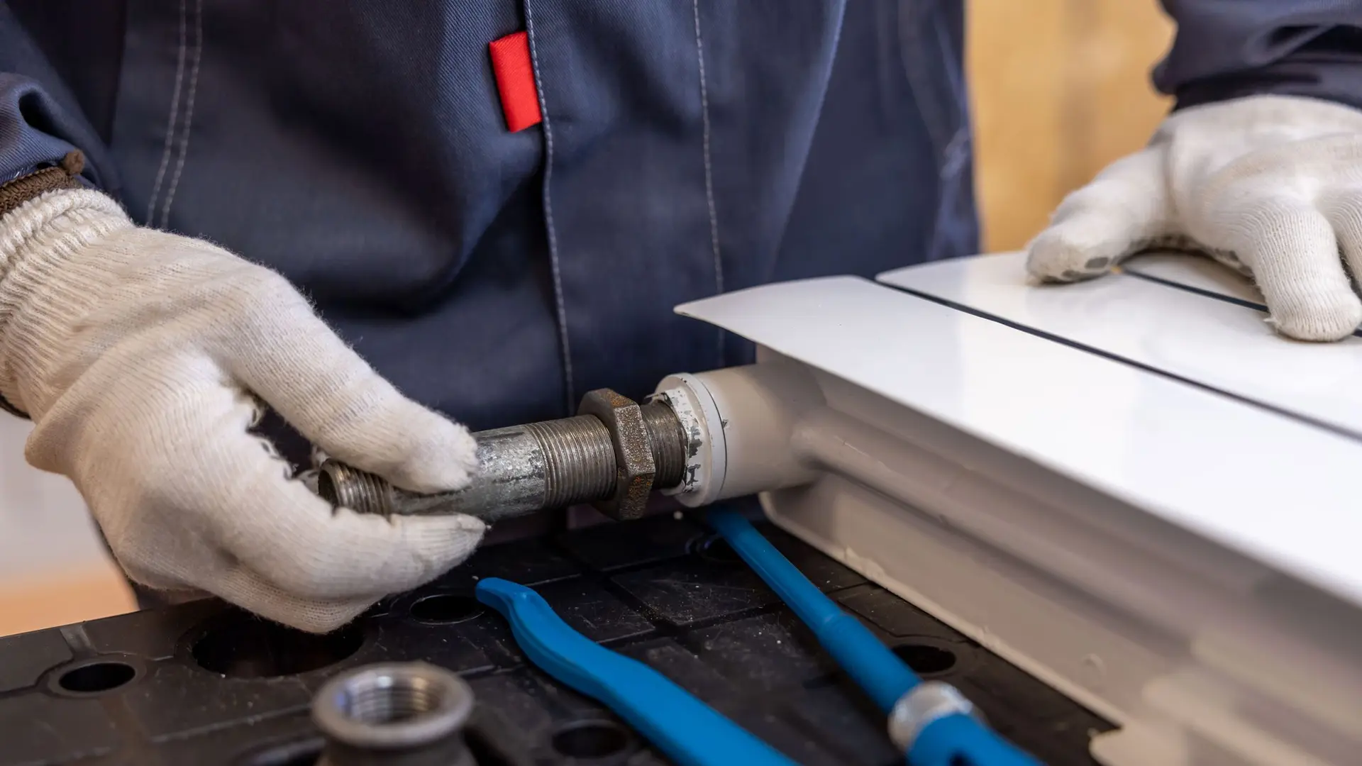 Gloved hands fitting a pipe to a radiator valve