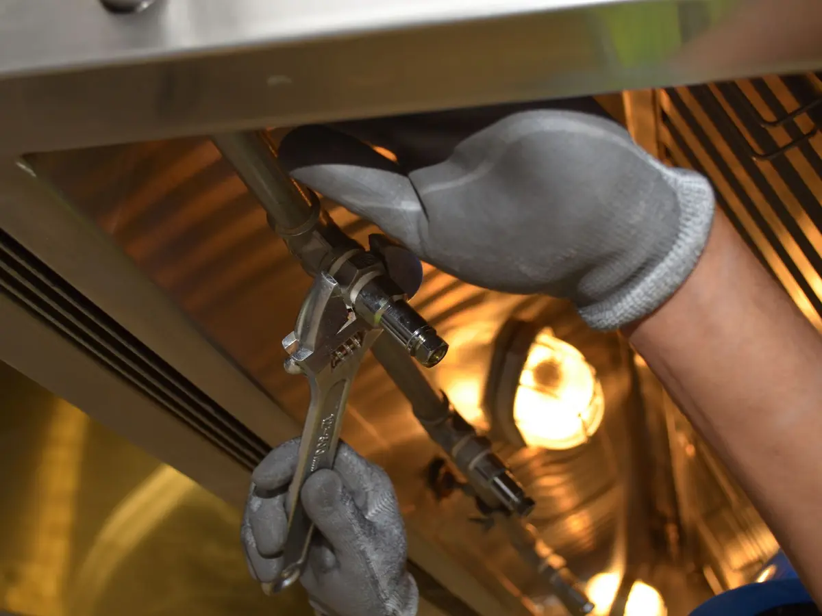 Adjusting a compression fitting with a spanner under a cooker hood