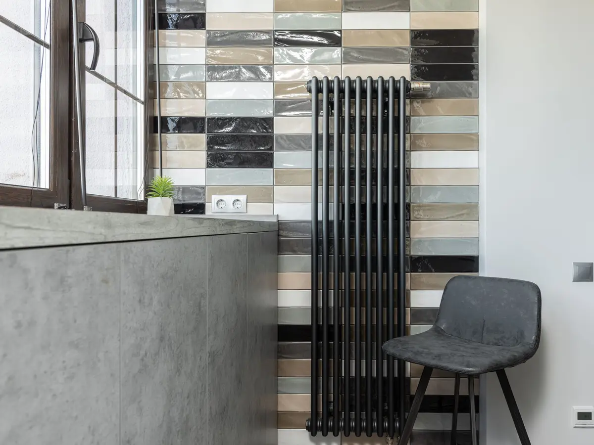 Tall black column radiator beside a tiled wall